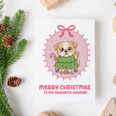 Christmas card with a dog holding a Christmas tree design, surrounded by festive elements on a white background.